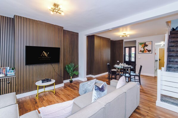A modern living room with a sofa, a dining table, and a TV mounted on a wooden wall. - Contractors | Families & Leisure | 3 Bed | Sleeps 6 | Bootle (Bootle)