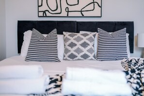 Ein Bett mit schwarzem Kopfteil, drei Kissen mit Muster und einer weißen Decke.