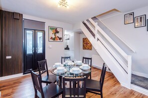 A dining area with a round table set for six, flanked by two black chairs, a staircase, and a kitchen in the background. - Contractors | Families & Leisure | 3 Bed | Sleeps 6 | Bootle (Bootle)