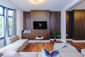 A modern living room with a flat-screen TV mounted on a wooden wall, a small round table with a chair, and a sofa with cushions. - Contractors | Families & Leisure | 3 Bed | Sleeps 6 | Bootle (Bootle)