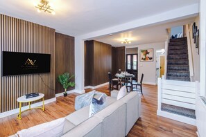 Un saló modern amb televisió de pantalla plana, un sofà, una zona de menjador i una escala.