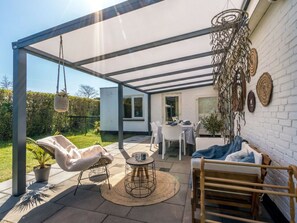 Ein überdachter Patio-Bereich mit Tisch und Stühlen, einer hängenden Pflanze und einem dekorativen Wandbild.