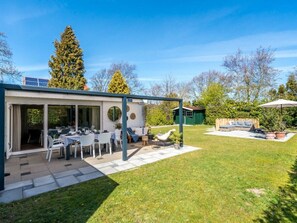 Ein moderner Essbereich im Freien mit Tischen und Stühlen, eine überdachte Sitzgelegenheit und ein Rasen-Hinterhof mit einer Holzterrasse und einer grünen Struktur.