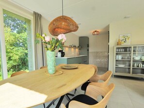 A dining area with a wooden table, chairs, a vase with flowers, and a hanging light fixture. - Holiday Home With 3 Bedrooms (Callantsoog)