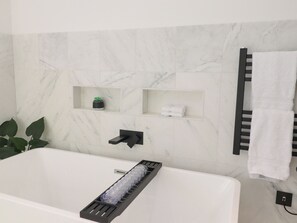 Ein modernes Badezimmer mit einer weißen Badewanne, einem Handtuchhalter und einem Regal mit einer Pflanze.