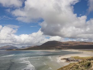 A coastal landscape with a beach, waves, and distant mountains under a partly cloudy sky. - Holm (Harris)