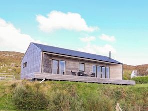 A modern house with a sloped roof, large windows, and a deck area. - Holm (Harris)