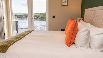 A hotel room with a bed, a view of the sea, and a framed picture on the wall.