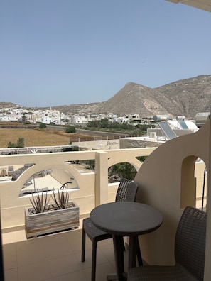 A balcony with a table and chairs, overlooking a town with white buildings and a mountain in the background. - Studio Apartment 'Double Room - 202' with Sea View, Wi-Fi and Air Conditioning (Εμπορείο)