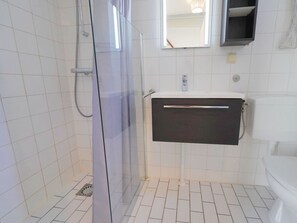 Ein Badezimmer mit einer Duschkabine aus Glas, einem weißen Waschbecken mit dunklem Unterschrank und einer weißen Toilette.
