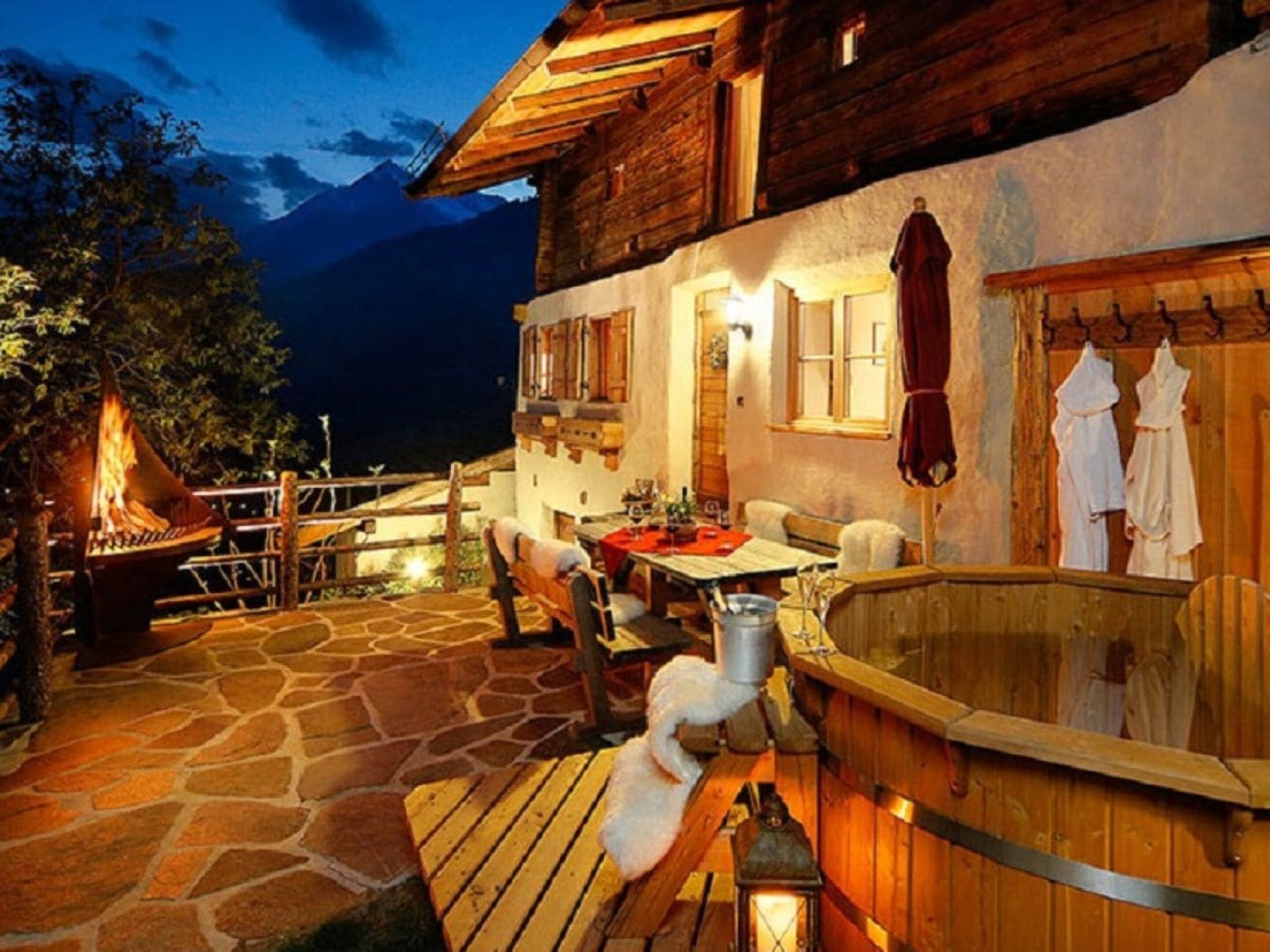 Un bâtiment rustique en bois, doté d’une terrasse en pierre, de sièges extérieurs et d’un jacuzzi.