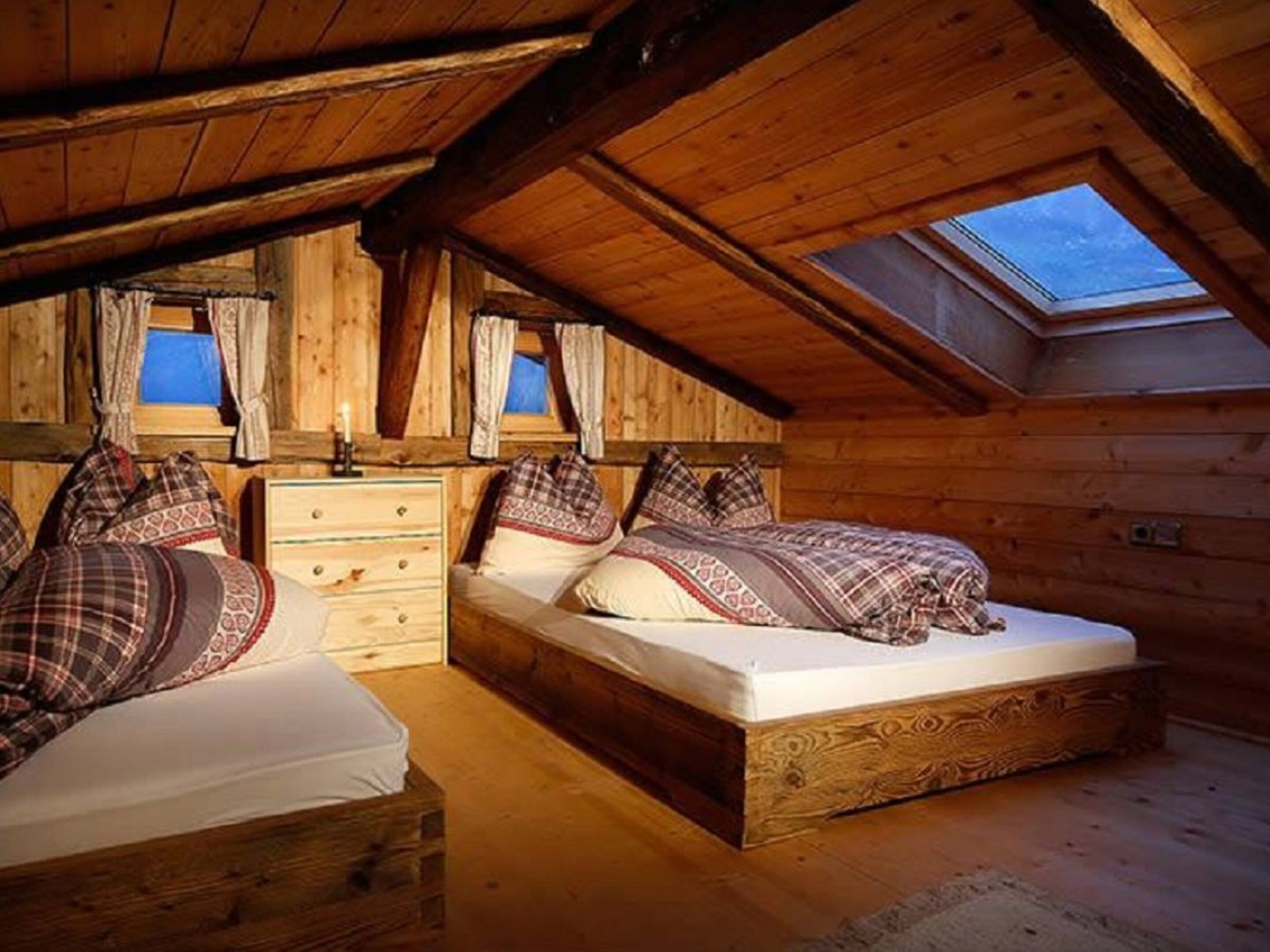 Une chambre mansardée chaleureuse, avec deux lits, une commode et une fenêtre de toit.