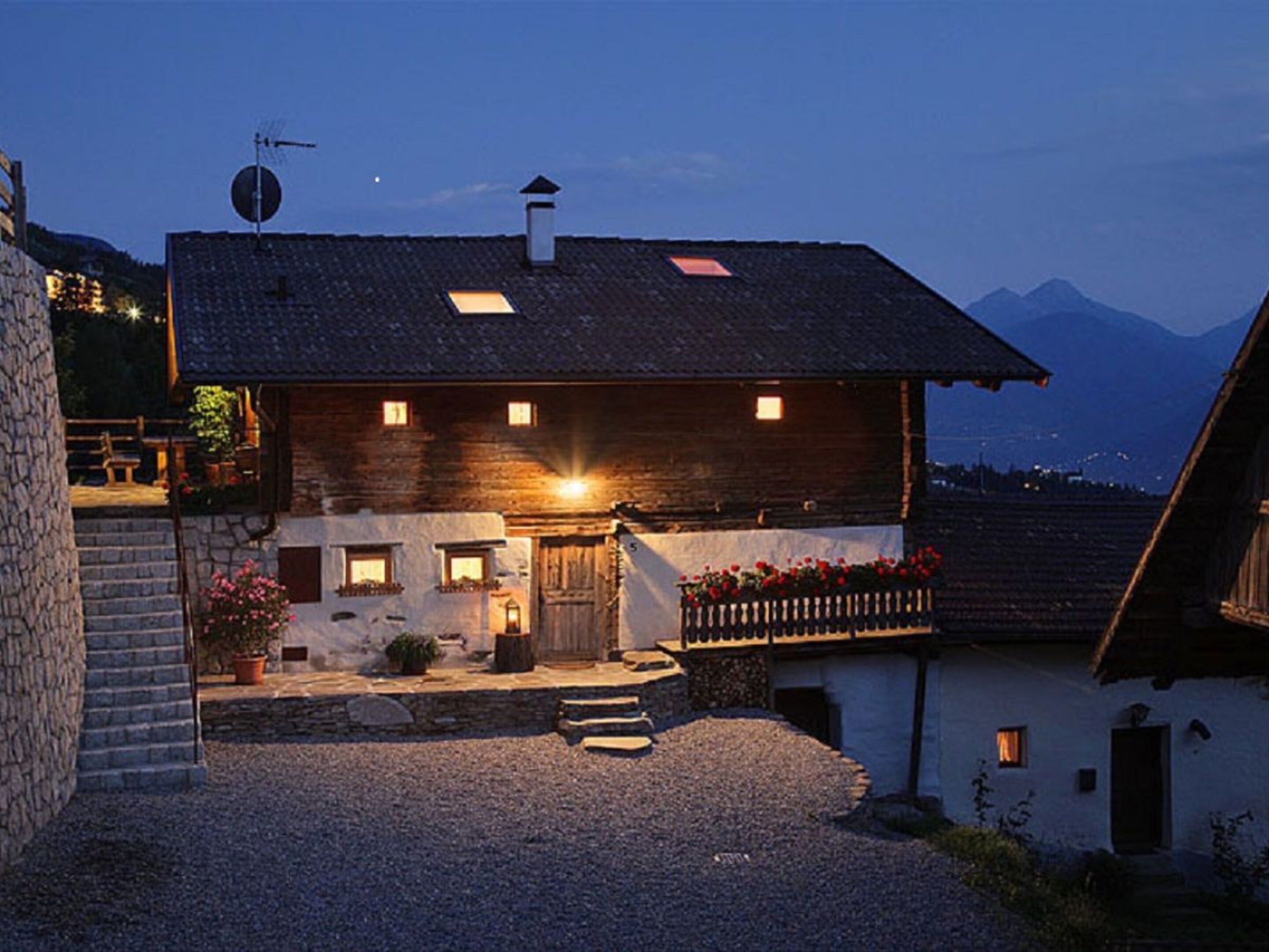Une maison de montagne rustique avec un escalier en pierre, une porte en bois et une allée gravillonnée.