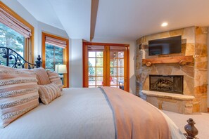 A bedroom with a large bed, a stone fireplace, and a view of the outdoors through a door. - Ski right out of the back door to a private trail on Deer Valley Resort! (Deer Valley)
