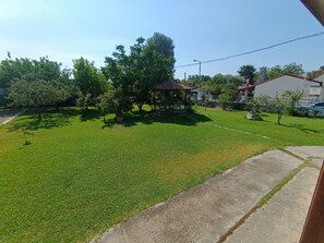 A grassy outdoor area with a gazebo, trees, and a building in the background.