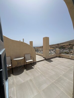 Una terraza en la azotea con una mesa y dos sillas, vista al paisaje y cielo despejado.