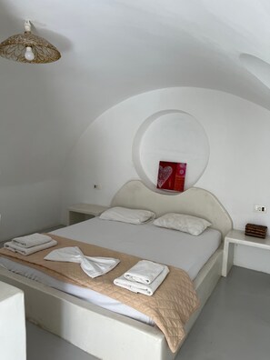 Un dormitorio con cama, ropa de cama blanca, una toalla, una mesita de noche y un elemento decorativo rojo.