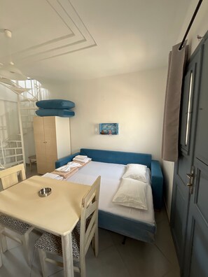 Ein gemütlicher Raum mit Bett, kleinem Tisch, Stuhl, Kleiderschrank und Wandregal.