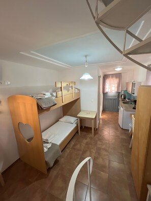 Ein kleines Zimmer mit Etagenbett, Tisch und einer Küchenzeile.