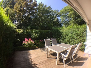Eine Terrass mit Tisch und Stühlen, umgeben von üppigem Grün und blühenden Pflanzen.