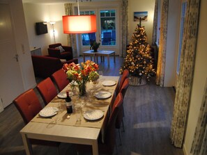 A dining area with a table set for two, a Christmas tree, and a television mounted on the wall. - Dunopark 1-6 (Oostkapelle)
