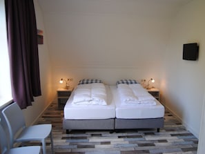 A double bed with a checkered pillow, bedside lamps, a chair, and a television on the wall. - Dunopark 1-6 (Oostkapelle)