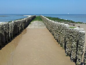 A coastal walkway with a stone wall on one side and a sandy path on the other, leading to the sea. - Dunopark 1-6 (Oostkapelle)