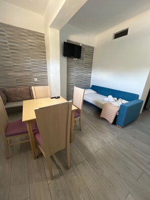 Ein modernes Zimmer mit Esstisch, Stühlen, einer Couch und einem an der Wand befestigten Fernseher.