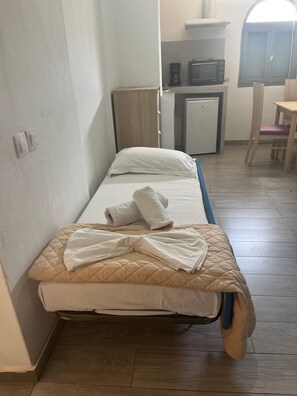 Un letto singolo con materasso trapuntato, un cuscino e asciugamani arrotolati.