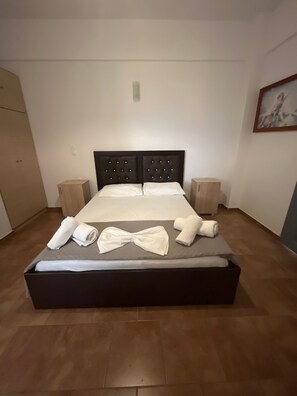 Ein ordentlich bezogenes Bett mit dunklem Kopfteil, zwei Nachttischen und einem Bild an der Wand.