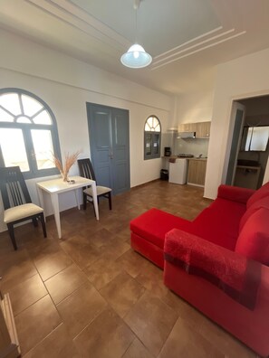 Ein Wohnzimmer mit einem roten Sofa, einem Esstisch mit Stühlen, einer Küchenzeile und einem großen Fenster mit Aussicht.