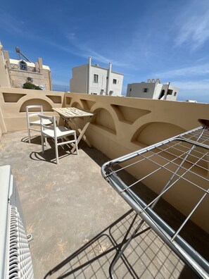 Eine Dachterrasse mit Tisch und Stühlen, einem Metallgeländer und Gebäuden im Hintergrund.