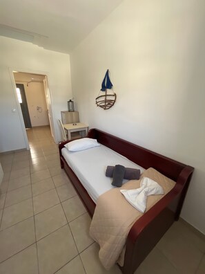 A single-bed room with a wooden frame, a white mattress, a beige blanket, and a blue towel. - Studio Apartment 'Triple Room - 103' with Sea View, Wi-Fi and Air Conditioning (Εμπορείο)