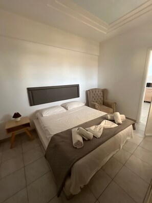 Ein Hotelzimmer mit einem großen Bett, einem Nachttisch mit Lampe, einem Sessel und Blick auf den Flur.