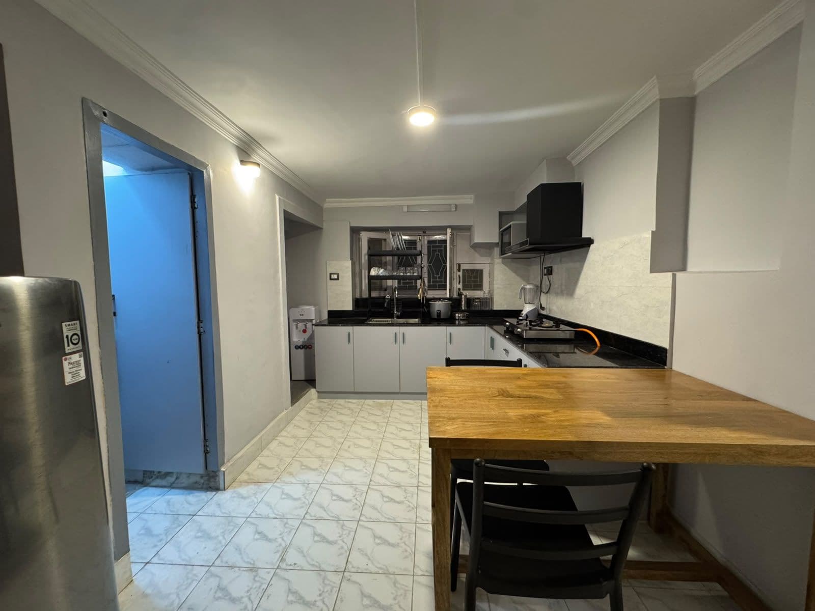A compact kitchen with a wooden table and chairs, a refrigerator, and a microwave.