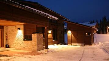 A wooden cabin with a stone foundation, a covered porch, and a snow-covered driveway.