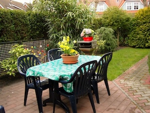 An outdoor patio with a table and chairs, surrounded by greenery and a brick pathway. - Holiday Apartment With 1 Bedroom (Zingst)