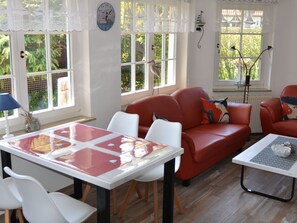A room with a red sofa, white chairs, a table with a red tablecloth, and a clock on the wall. - Holiday Apartment With 1 Bedroom (Zingst)