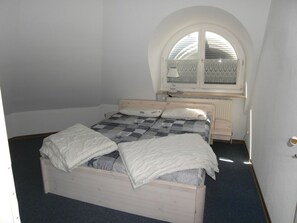 A single-bed room with a wooden headboard, a checkered bedspread, a bedside table with a lamp, and a window with decorative curtains. - Holiday Apartment With 1 Bedroom (Zingst)