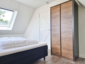 Ein Schlafzimmer mit Bett, Schrank, Dachfenster und weißer Tür.
