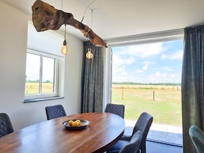 Ein Essbereich mit einem Holztisch, vier Stühlen, einer Obstschale und einem großen Fenster mit Blick auf ein Feld.