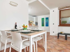A dining area with a wooden table, white chairs, and a kitchen in the background. - "casa Appartamenti Alin A" (Malcesine)