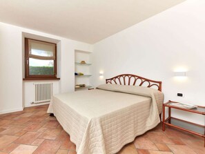 A bedroom with a bed, a window, a radiator, shelves, and a bedside table. - "casa Appartamenti Alin A" (Malcesine)