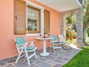 An outdoor patio with two white chairs and a table, a stone floor, and a peach-colored wall with wooden shutters. - "casa Appartamenti Alin A" (Malcesine)