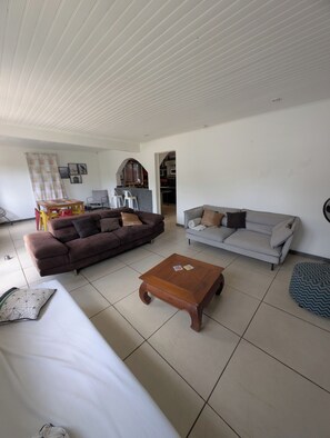 Ein Wohnzimmer mit einem braunen Sofa, einem grauen Sofa, einem Holztisch und einem gestreiften Hocker.