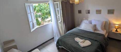 A bedroom with a bed, a sofa, a window with curtains, a ceiling fan, and a bedside lamp.