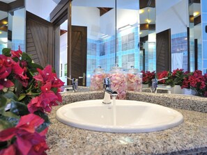 Ein Hotelbad mit einer Granittheke, einem weißen Waschbecken und zwei Glasvasen mit rosa Blumen.