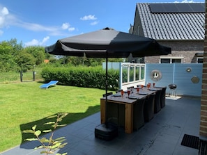 Eine Terrasse im Freien mit einem Esstisch, einem Grill und einem blauen Liegestuhl.
