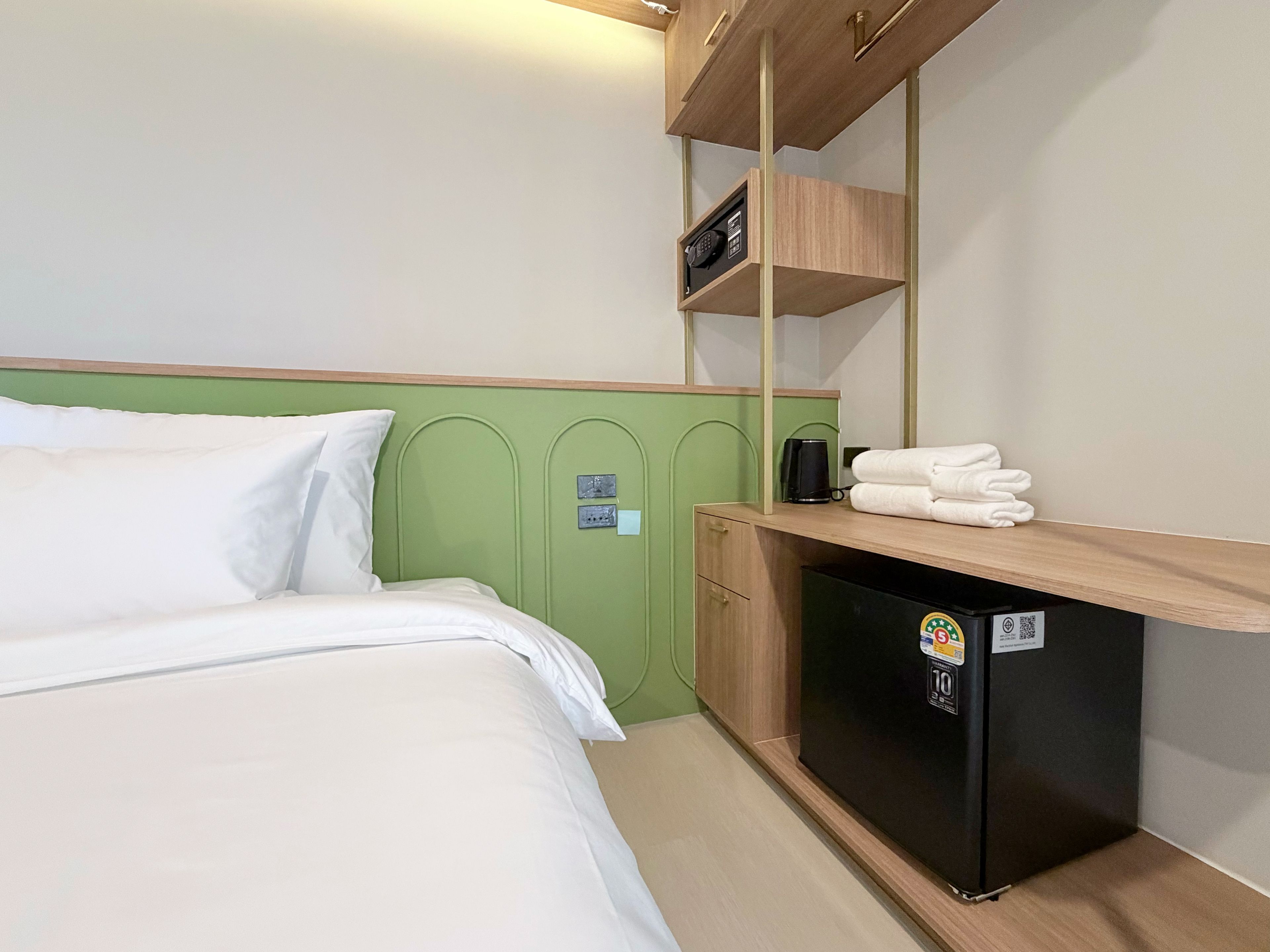 Una habitación de hotel con una cama, un pequeño escritorio con refrigerador y un estante encima del escritorio.