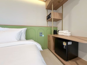 Una habitación de hotel con una cama, un pequeño escritorio con refrigerador y un estante encima del escritorio.